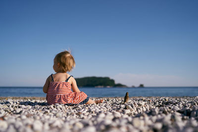 Rear view of boy on pebbles at beach against clear sky