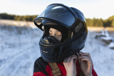 Close-up of teenage boy wearing helmet on snow covered field against sky