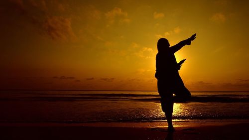 Silhouette man standing on beach against sky during sunset