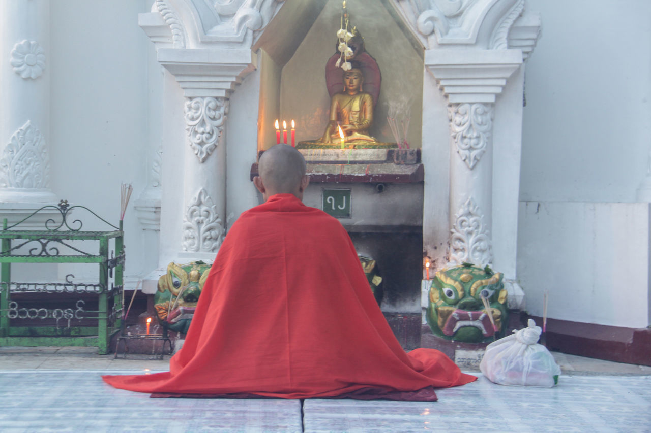 REAR VIEW OF MAN SITTING ON TEMPLE OUTSIDE BUILDING