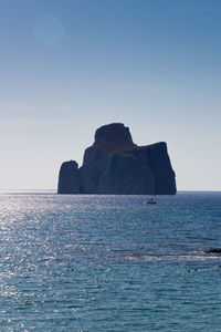 Rock formation in sea against clear blue sky