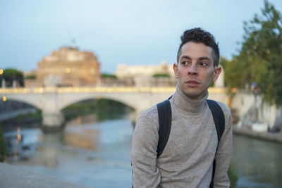 Portrait of young man standing against bridge in city