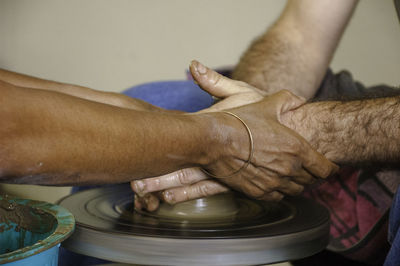 Cropped image of person assisting man while molding shape on pottery wheel