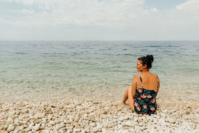 Woman sitting at beach against sky