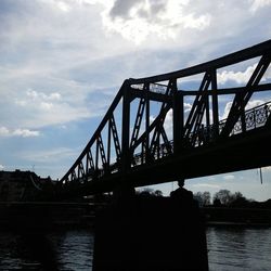 Silhouette of bridge over river against cloudy sky