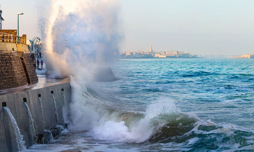 Waves splashing on promenade against sky