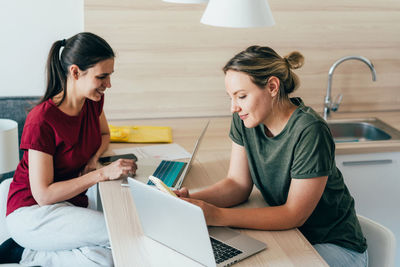 Two female coworkers working using laptops in the kitchen