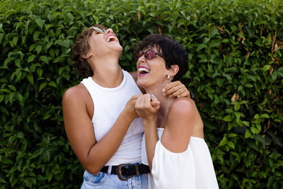 Happy friends standing against green plants