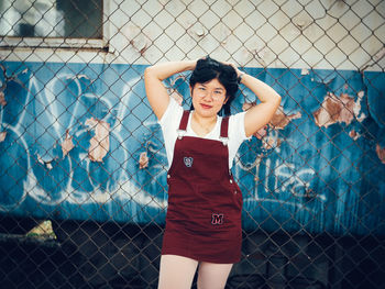Portrait of young woman standing by chainlink fence