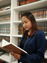 Young woman holding book while standing at home