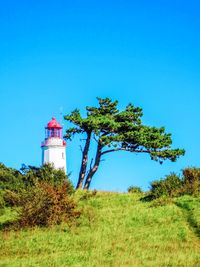 Lighthouse on field against clear blue sky