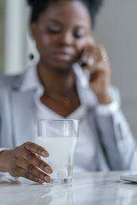 Ill woman holding glass with medicine by laptop on table