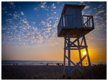 Lifeguard hut on beach against sky during sunset