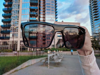 Reflection of person on sunglasses against sky in city
