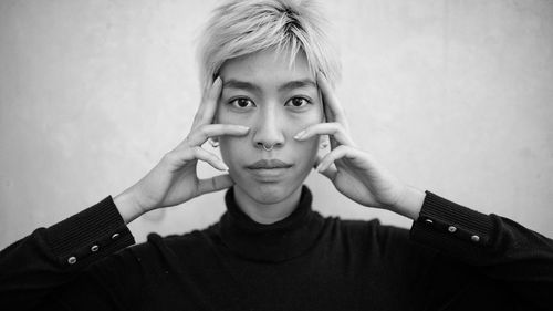 Portrait of woman touching cheek against wall