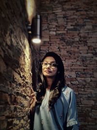 Portrait of smiling young woman standing against brick wall