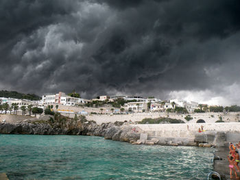 Buildings by sea against storm clouds