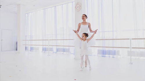 Young woman teaching ballet dance to girl in studio