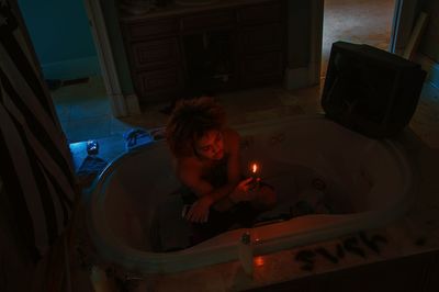 High angle view of young woman holding lit candle in darkroom