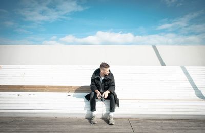 Full length of young man sitting on steps against sky