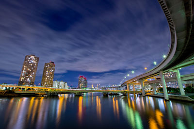 Illuminated bridge over river by buildings against sky at night