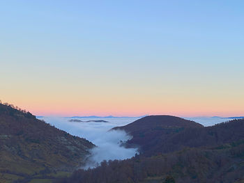 Scenic view of fogy mountains against clear sky during sunset