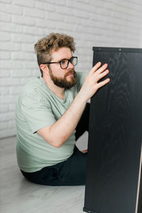 Side view of young man using digital tablet while standing against wall