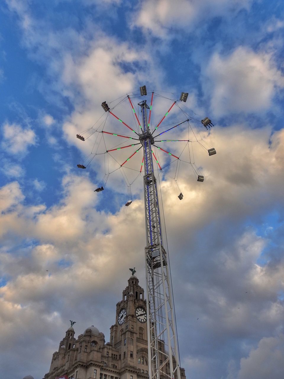 low angle view, sky, cloud - sky, built structure, architecture, arts culture and entertainment, cloud, tall - high, tower, amusement park ride, blue, amusement park, building exterior, day, tall, travel destinations, outdoors, development, high section, chain swing ride, no people, tourism, cloudy, spire, cumulus cloud