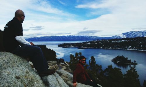 Rear view of man sitting on bench by lake