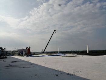 View of factory at harbor against cloudy sky
