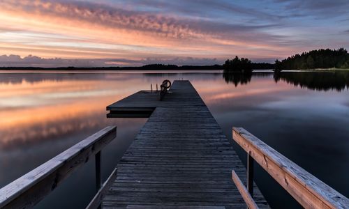 Jetty over lake against cloudy sky during sunset