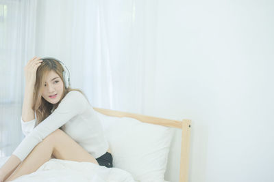 Young woman with headphones sitting on bed