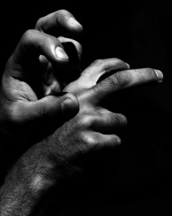 Close-up of father holding baby hand against black background