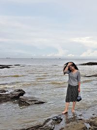 Woman standing at beach against cloudy sky