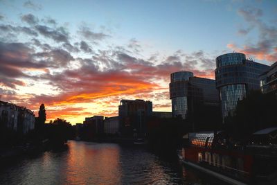 Buildings by river against sky during sunset