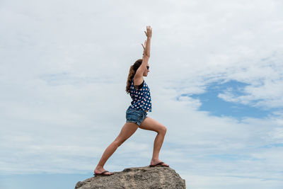 Low angle view of woman exercising on rock against sky