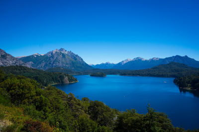 Scenic view of lake and mountains against clear blue sky