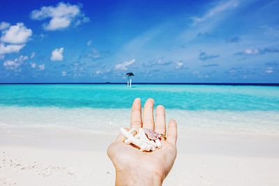 Midsection of person hand on beach against blue sky