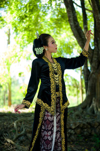 Full length of young woman standing against tree