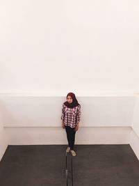 Full length of young woman standing against wall