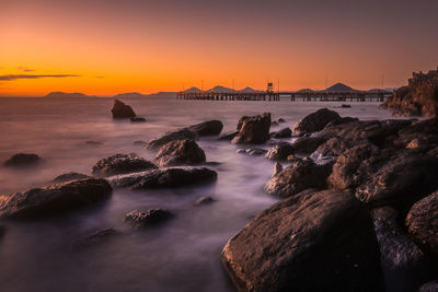 Rocks in sea against sky during sunset