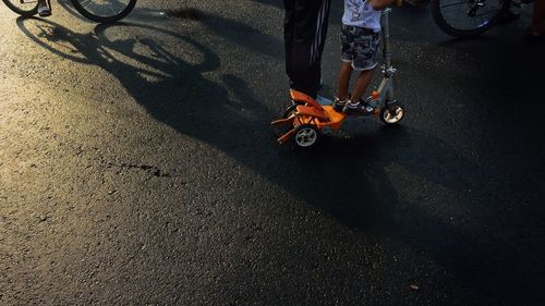 Low section of father standing by son on push scooter on road