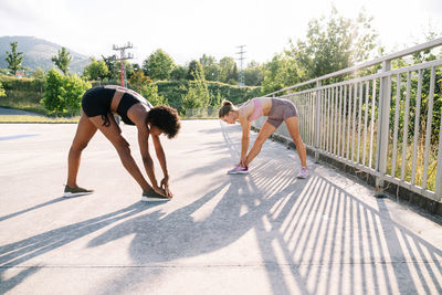 Full body of determined young multiethnic sportswomen doing squat exercise with resistance band during fitness workout in park in summer day