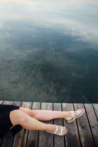 Low section of woman sitting on wood against sea