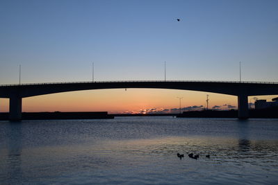 Silhouette birds on bridge over river against sky during sunset