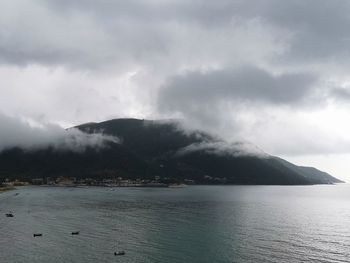 Scenic view of sea by mountain against sky