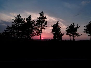 Silhouette trees on landscape against sky at sunset