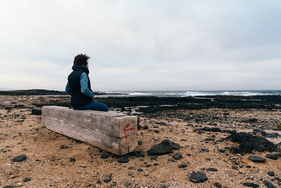 Rear view of woman standing on rock at beach against sky