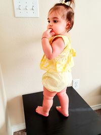 Cute baby girl looking away standing on table against wall at home