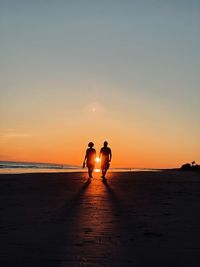 Silhouette people on beach against sky during sunset